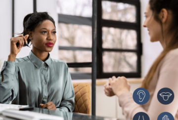 Two women engaged in an assessment dialogue, one serving as the Assessor, in a private office space. The learner has a visual impairment. so the Assessor is providing support and guidance