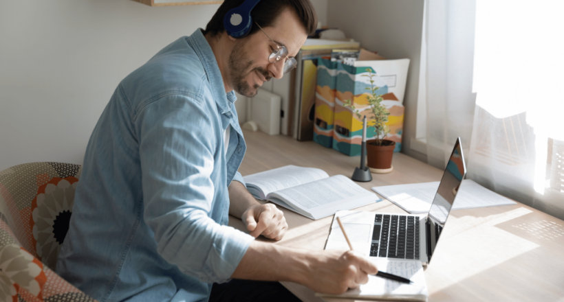 man-working-at-desk-on-laptop-writing-notepad-laptop